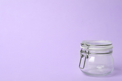 Photo of Closed empty glass jar on lilac background, space for text
