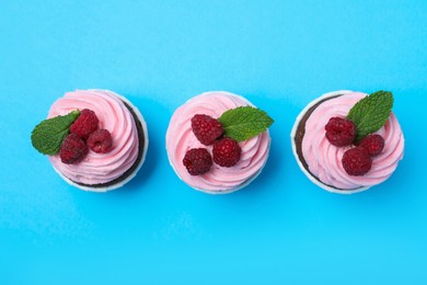 Delicious cupcakes with cream and raspberries on light blue background, flat lay