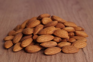 Photo of Pile of delicious almonds on wooden table, closeup