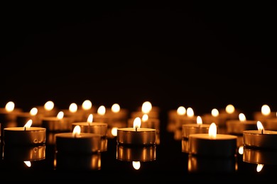 Photo of Burning candles on mirror surface in darkness, space for text