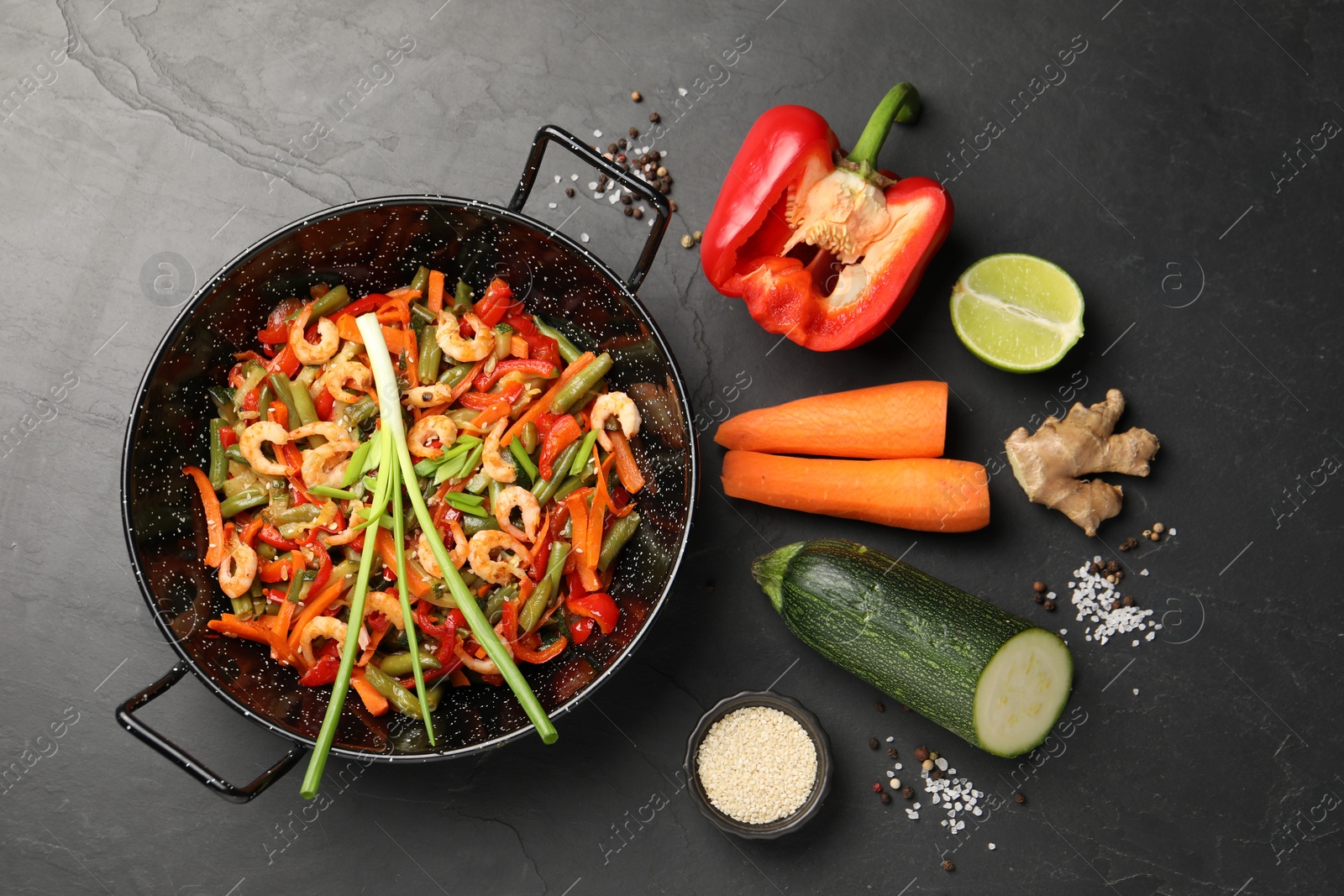 Photo of Shrimp stir fry with vegetables in wok and ingredients on black table, flat lay