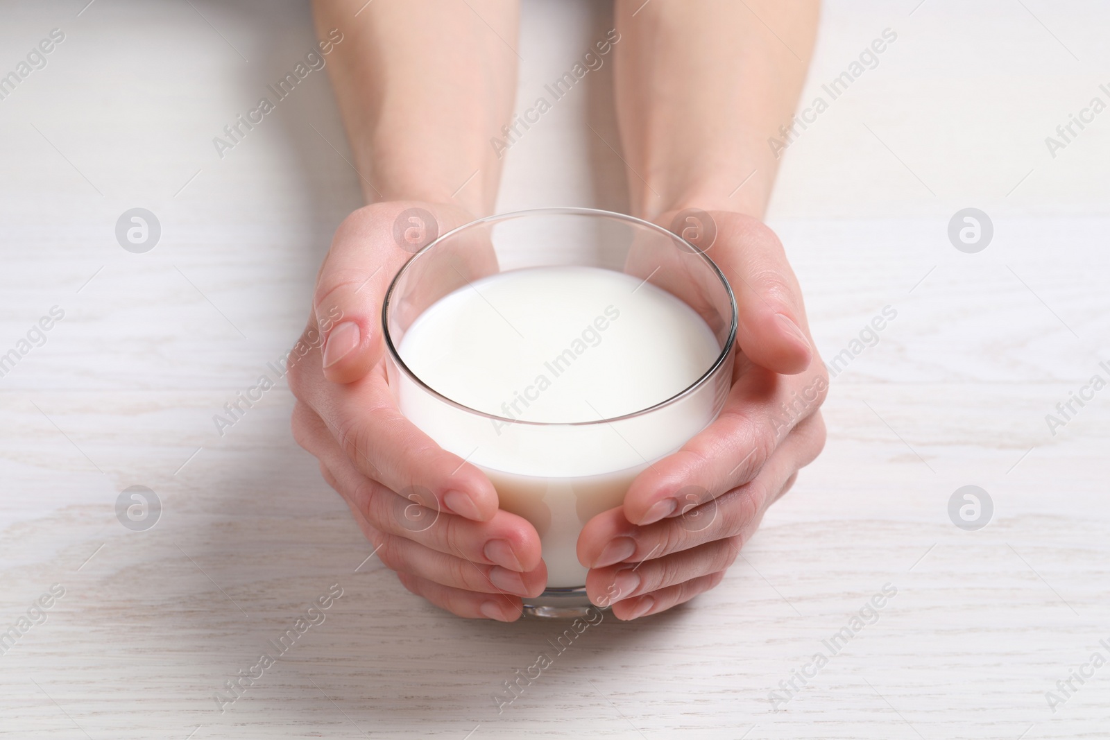 Photo of Woman holding glass of milk at white wooden table, closeup