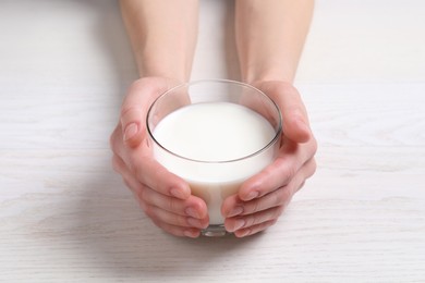 Photo of Woman holding glass of milk at white wooden table, closeup