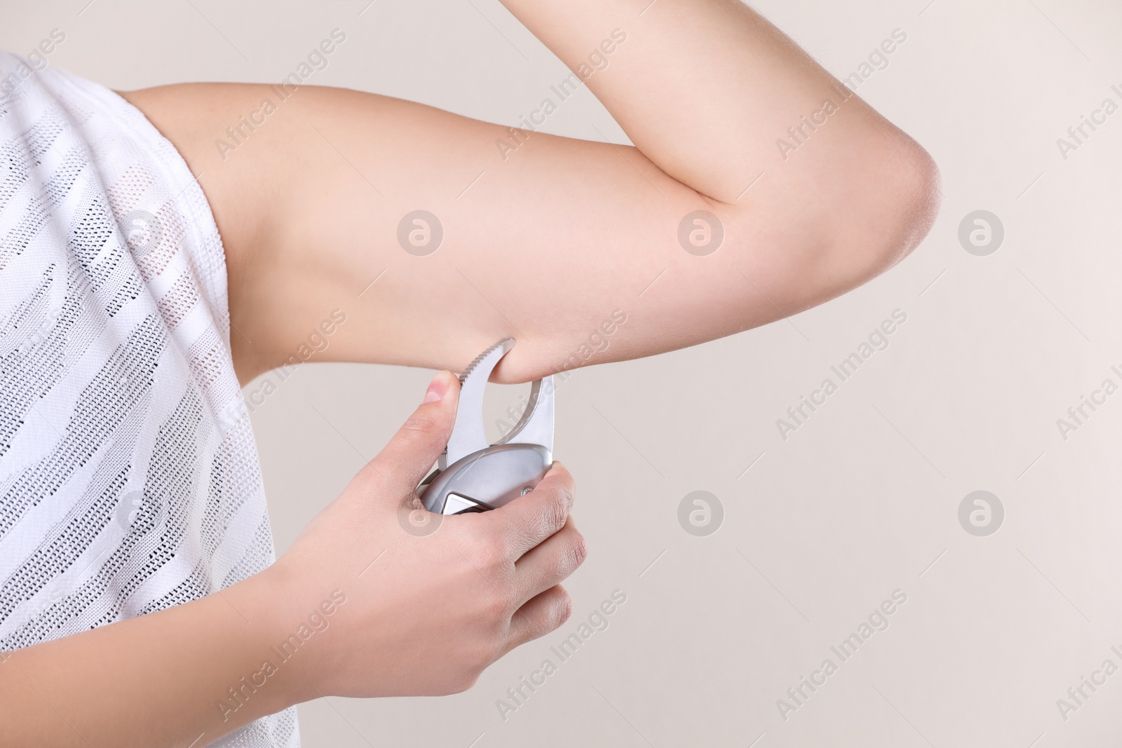 Photo of Young woman measuring body fat with caliper on beige background, closeup. Nutritionist's tool