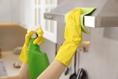 Photo of Woman with spray bottle and microfiber cloth cleaning kitchen hood indoors, closeup