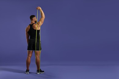 Photo of Muscular man exercising with elastic resistance band on purple background, back view. Space for text