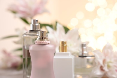 Bottles of perfume against beautiful lily flowers and blurred lights, closeup. Space for text