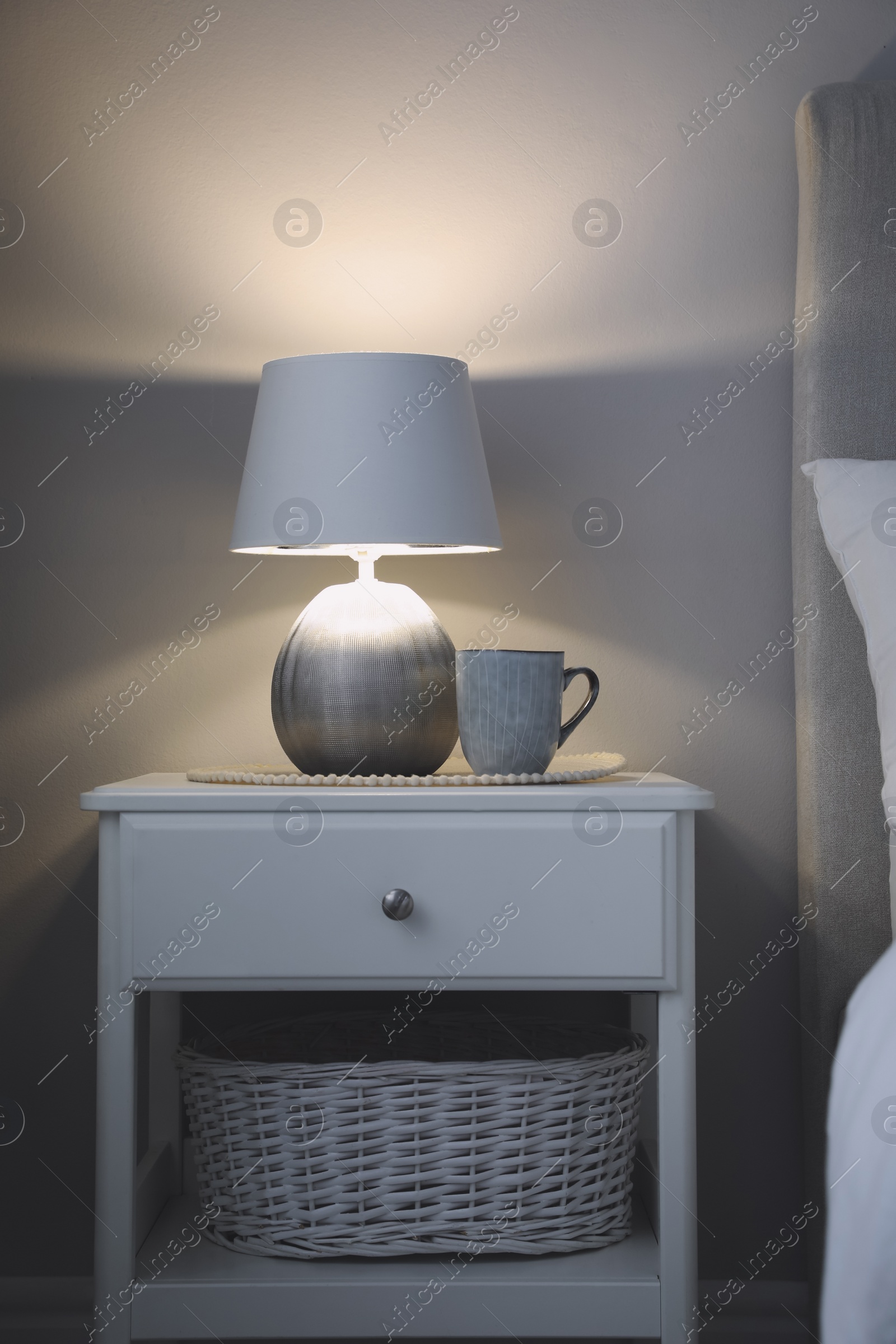 Photo of Stylish lamp and cup of drink on white nightstand in room