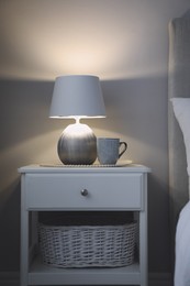 Stylish lamp and cup of drink on white nightstand in room