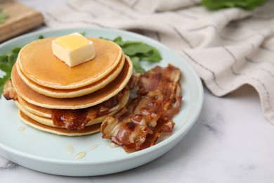 Photo of Tasty pancakes with butter, fried bacon and fresh arugula on white marble table, closeup