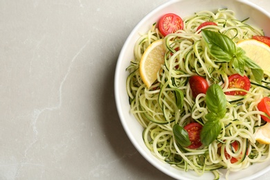 Photo of Delicious zucchini pasta with cherry tomatoes, lemon and basil on light grey table, top view. Space for text