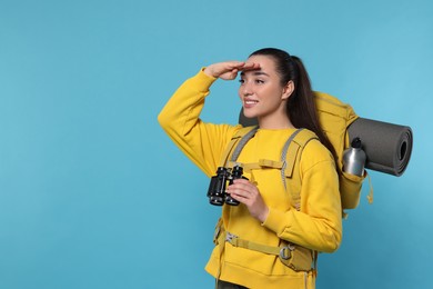 Photo of Young woman with backpack and binoculars on light blue background, space for text. Active tourism