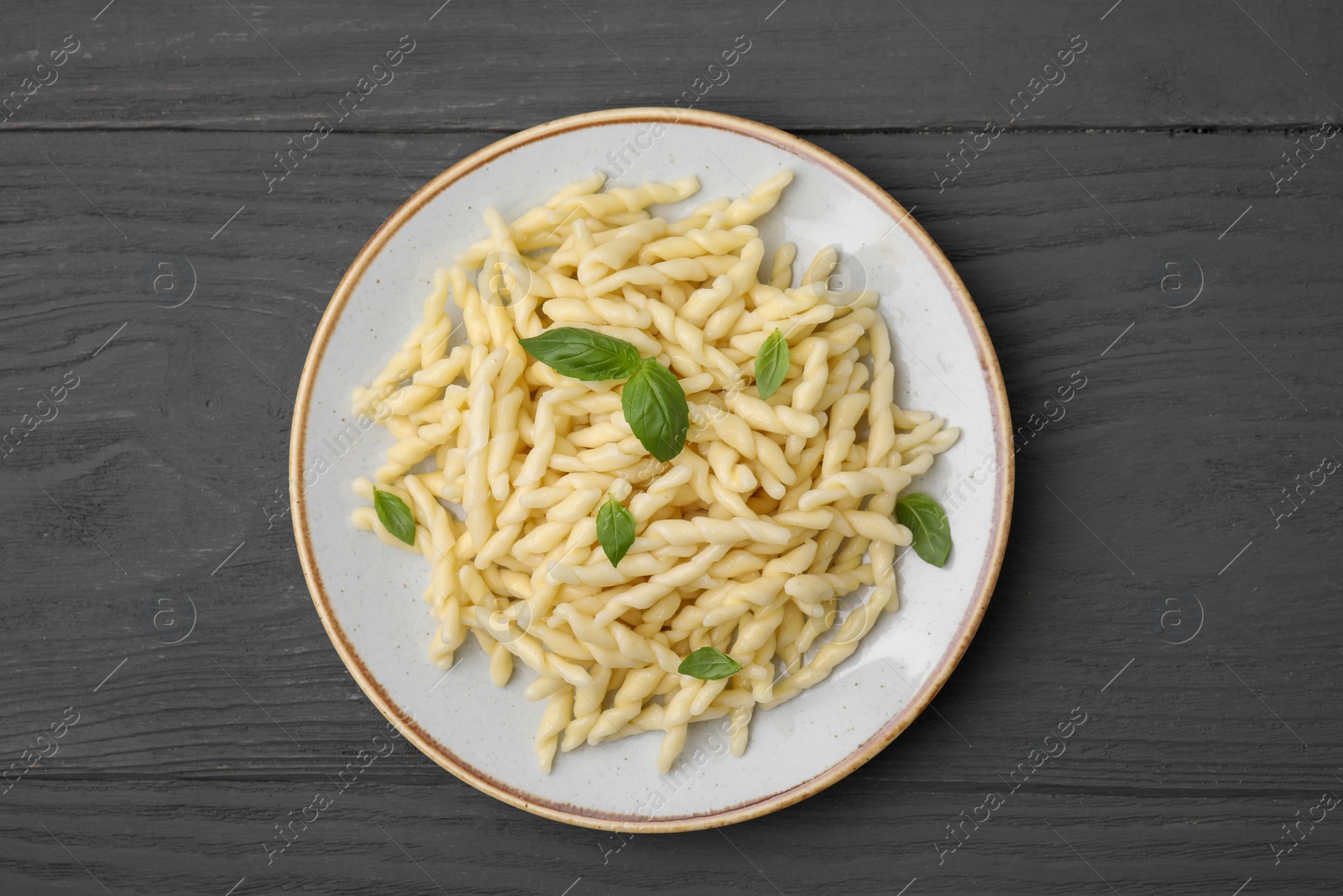 Photo of Plate of delicious trofie pasta with basil leaves on grey wooden table, top view
