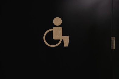Image of Special needs accessible public toilet sign on black door, closeup. Wheelchair symbol
