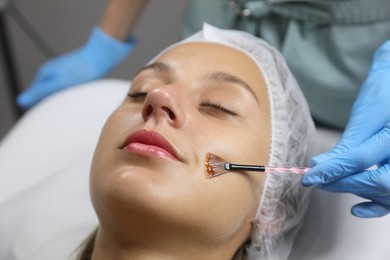 Photo of Cosmetologist applying chemical peel product on client's face in salon