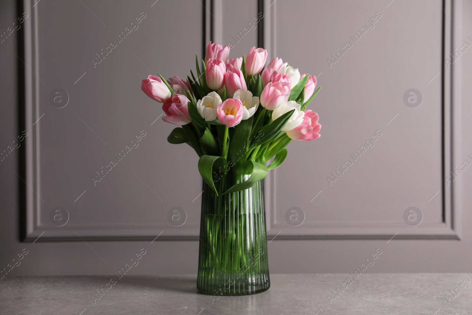 Photo of Beautiful bouquet of tulips in glass vase on grey table