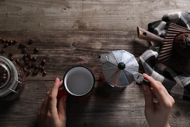 Photo of Woman holding moka pot with coffee and cup at wooden table, top view. Space for text