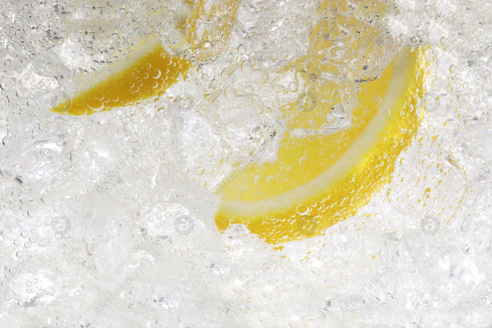 Photo of Juicy lemon slices and ice cubes in soda water against white background, closeup