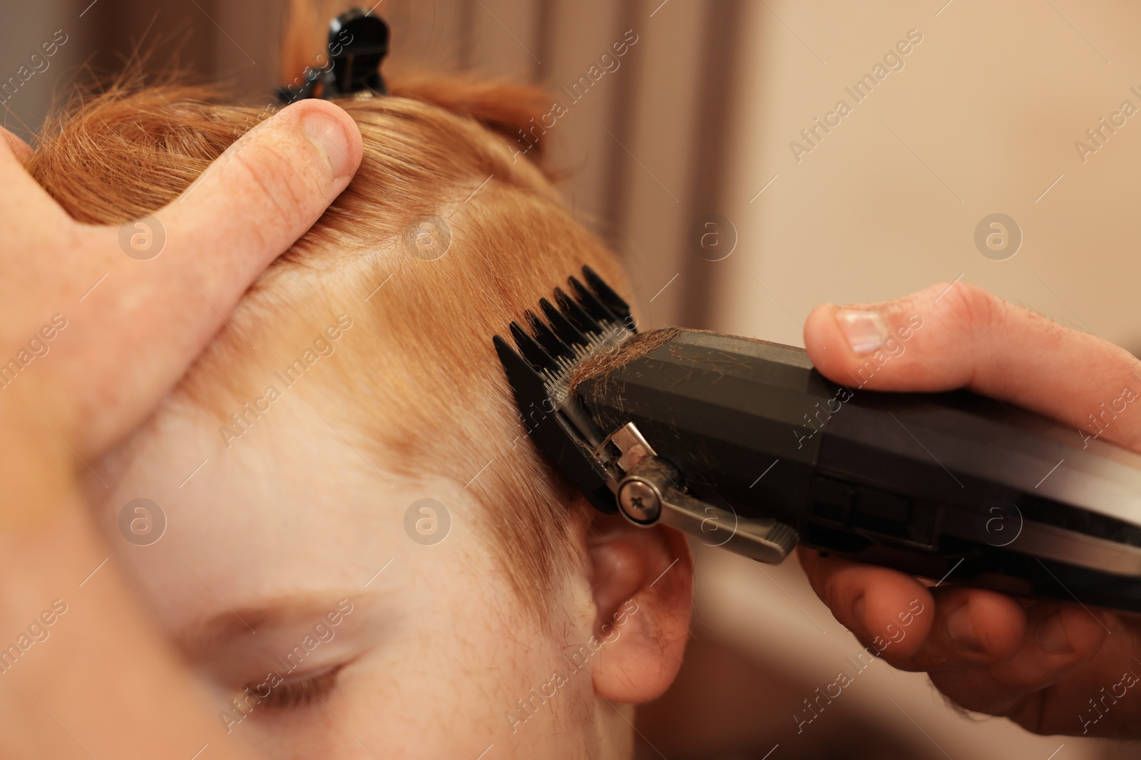 Photo of Professional hairdresser cutting boy's hair in beauty salon, closeup