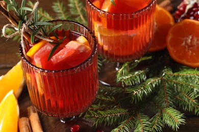 Photo of Christmas Sangria cocktail in glasses, ingredients and fir tree branches on wooden table, closeup