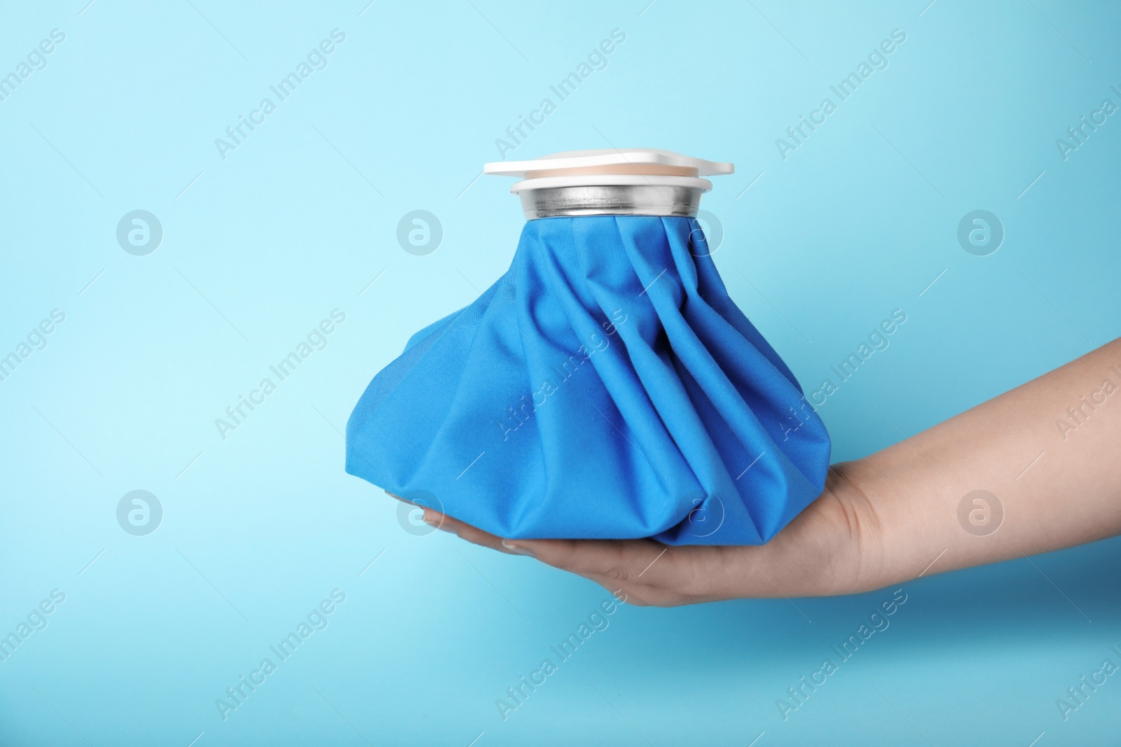 Photo of Woman holding ice pack against blue background, closeup
