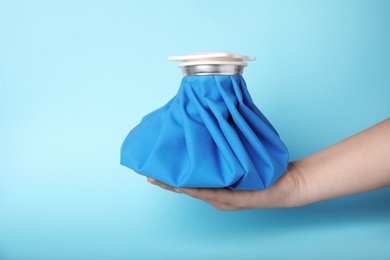 Woman holding ice pack against blue background, closeup