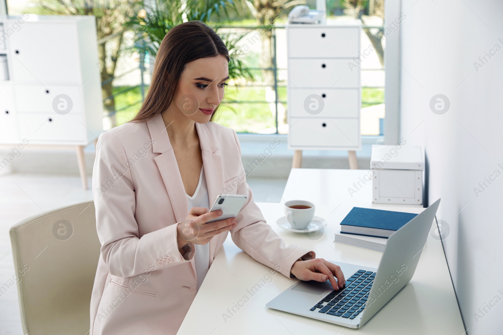 Image of Young woman using phone and laptop in office