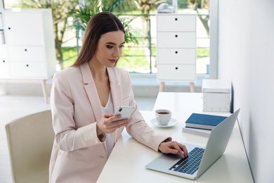 Young woman using phone and laptop in office