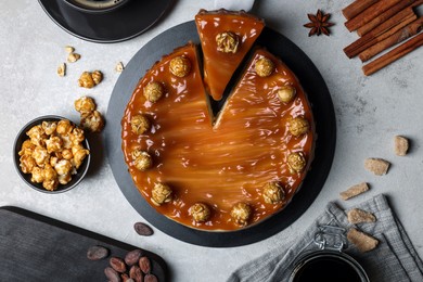 Sliced delicious caramel cheesecake with popcorn served on light grey table, flat lay