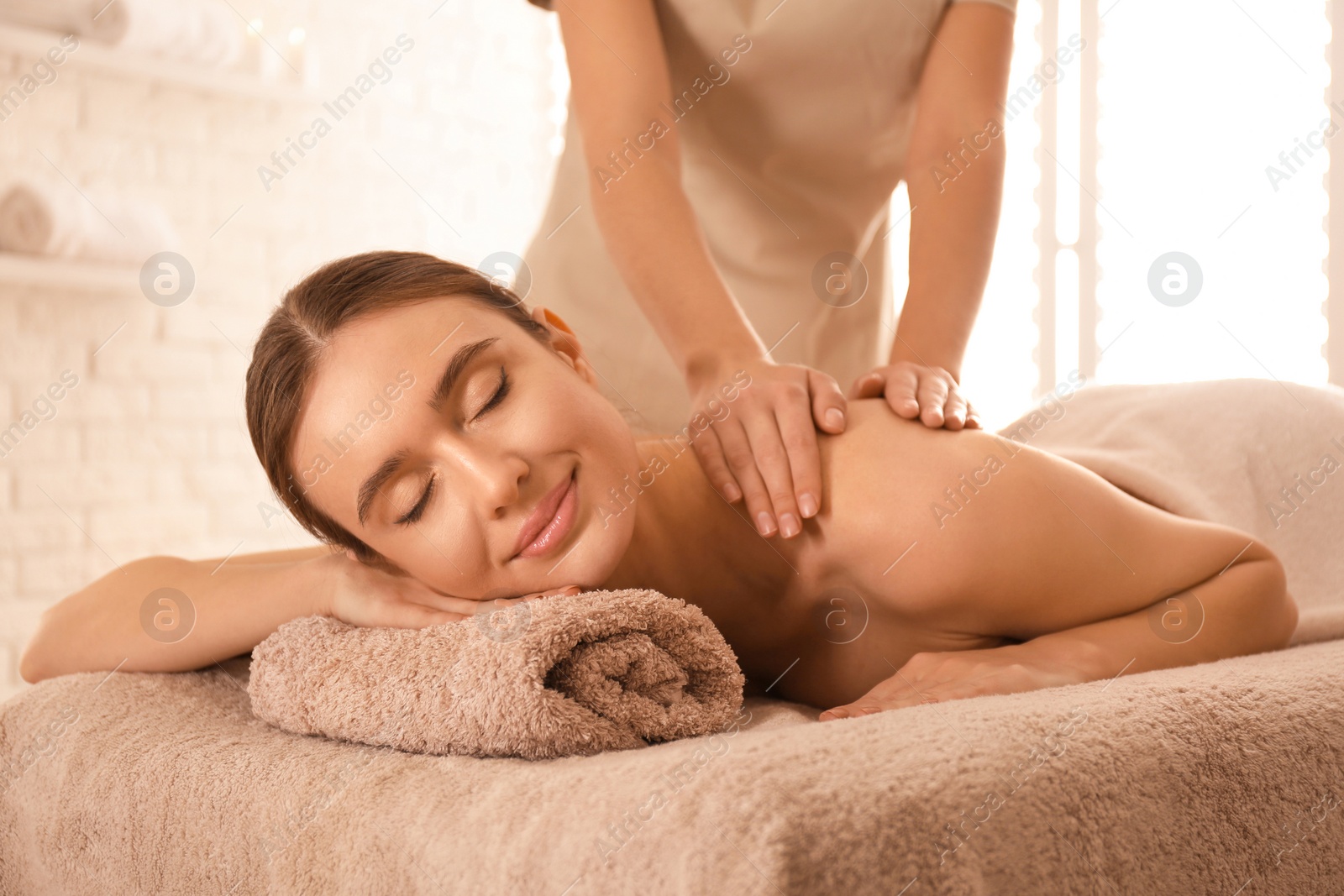 Photo of Young woman having body scrubbing procedure with sea salt in spa salon