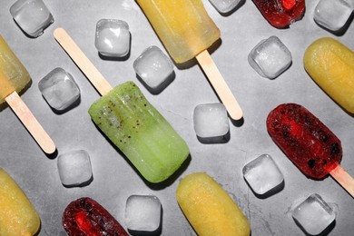 Photo of Delicious pops and ice cubes on grey table, flat lay. Fruit popsicle