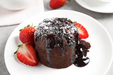 Delicious warm chocolate lava cake with mint and strawberries on table, closeup