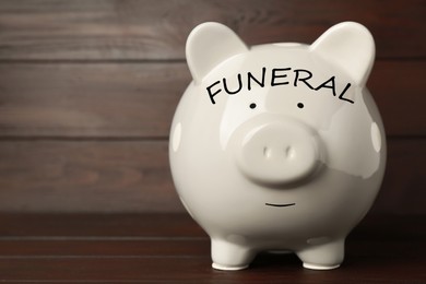 Image of Money for funeral expenses. White piggy bank on wooden table. Space for text