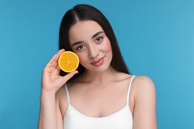 Photo of Beautiful young woman with piece of orange on light blue background