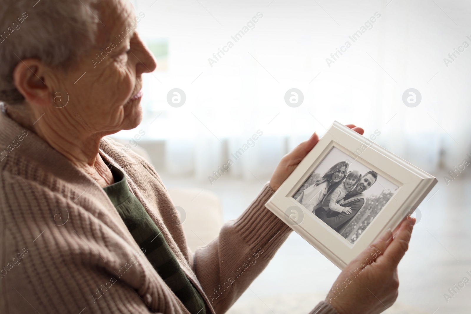 Photo of Elderly woman with framed family portrait at home