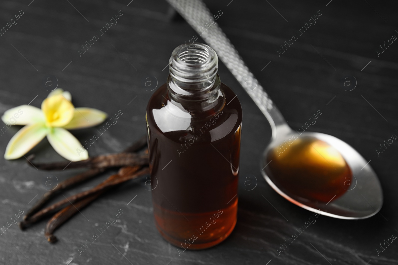 Photo of Aromatic homemade vanilla extract on black table, closeup