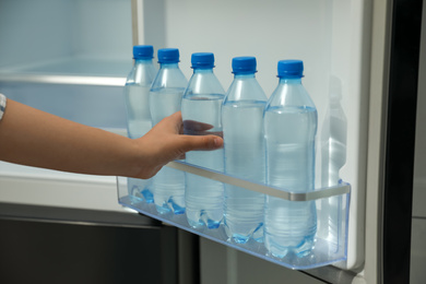 Photo of Woman taking bottle of fresh water from fridge door bin, closeup