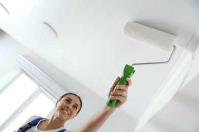 Photo of Worker painting ceiling with white dye indoors, focus on roller