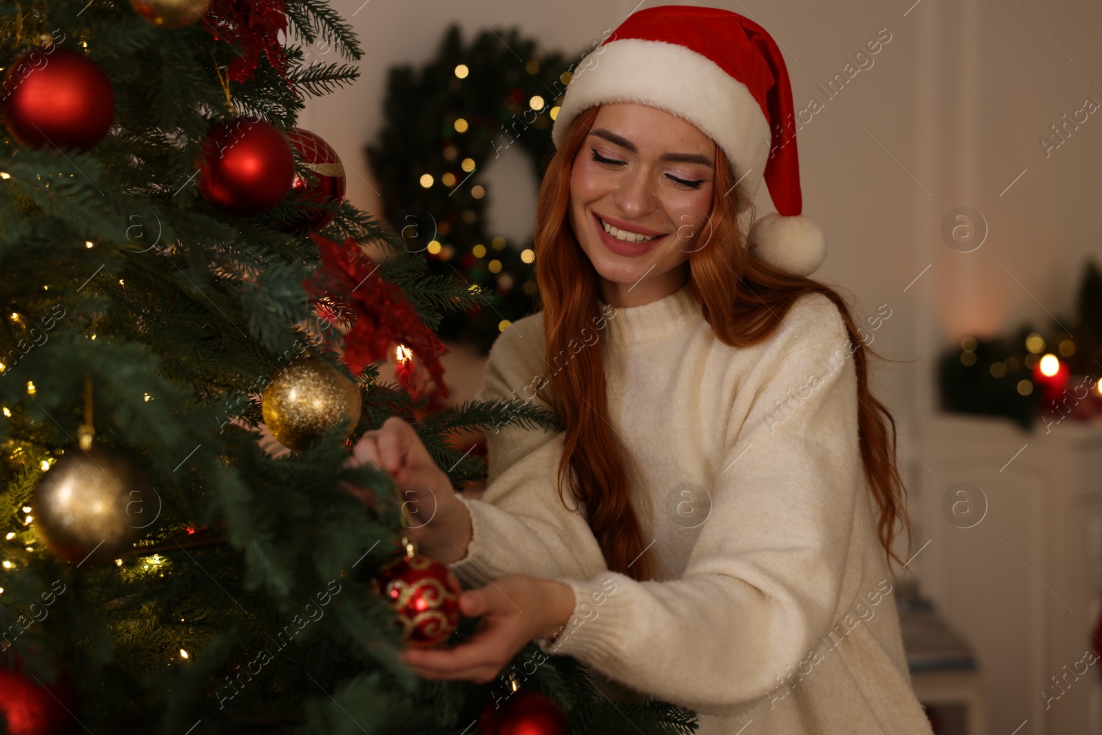 Photo of Happy young woman in Santa hat decorating Christmas tree at home