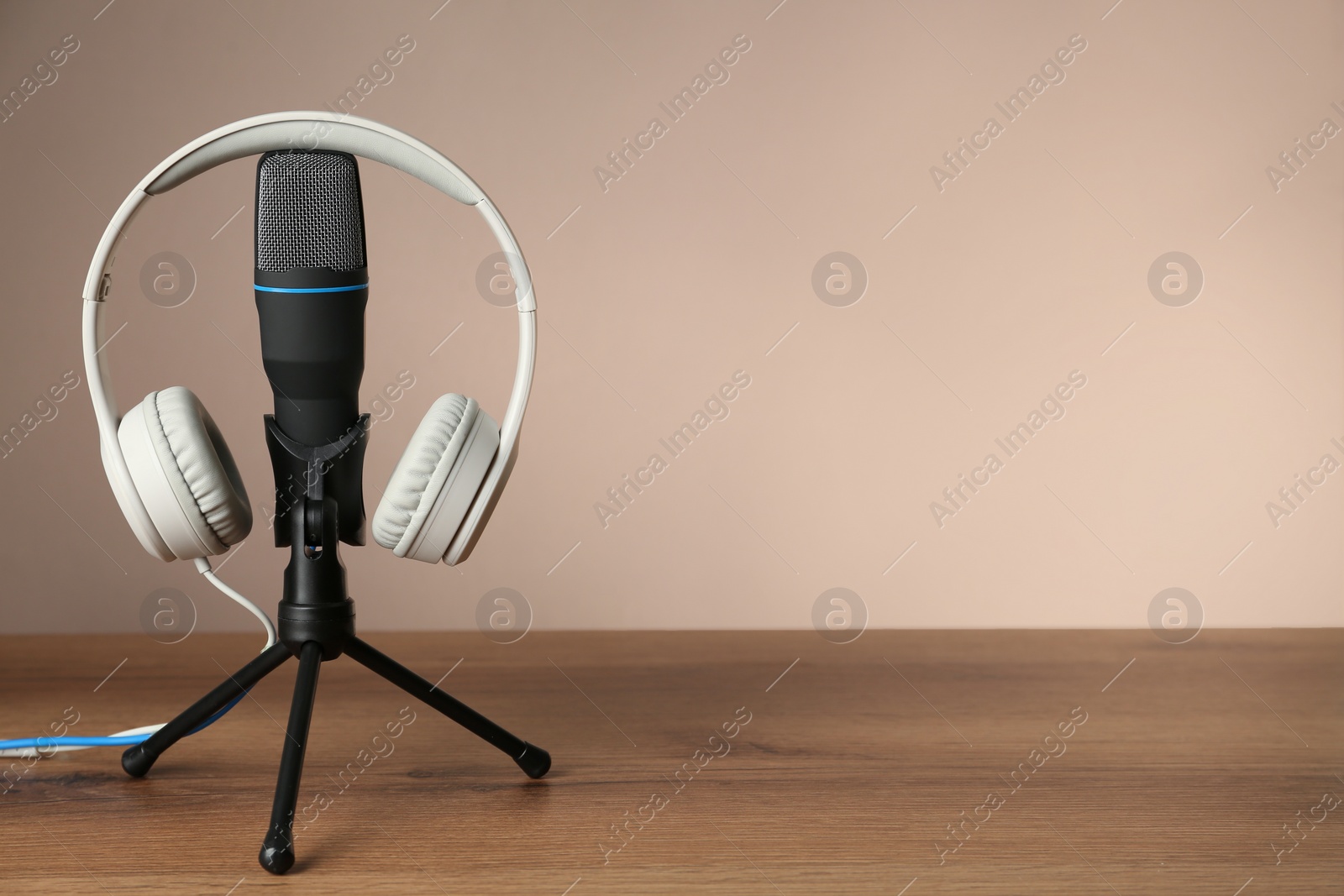 Photo of Microphone and modern headphones on wooden table against beige background, space for text