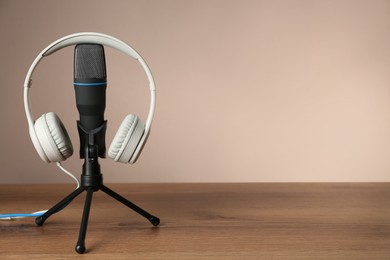 Microphone and modern headphones on wooden table against beige background, space for text