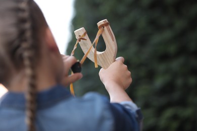 Photo of Little girl playing with slingshot outdoors, closeup