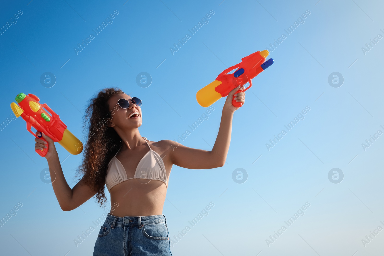 Photo of African American woman with water guns having fun against blue sky