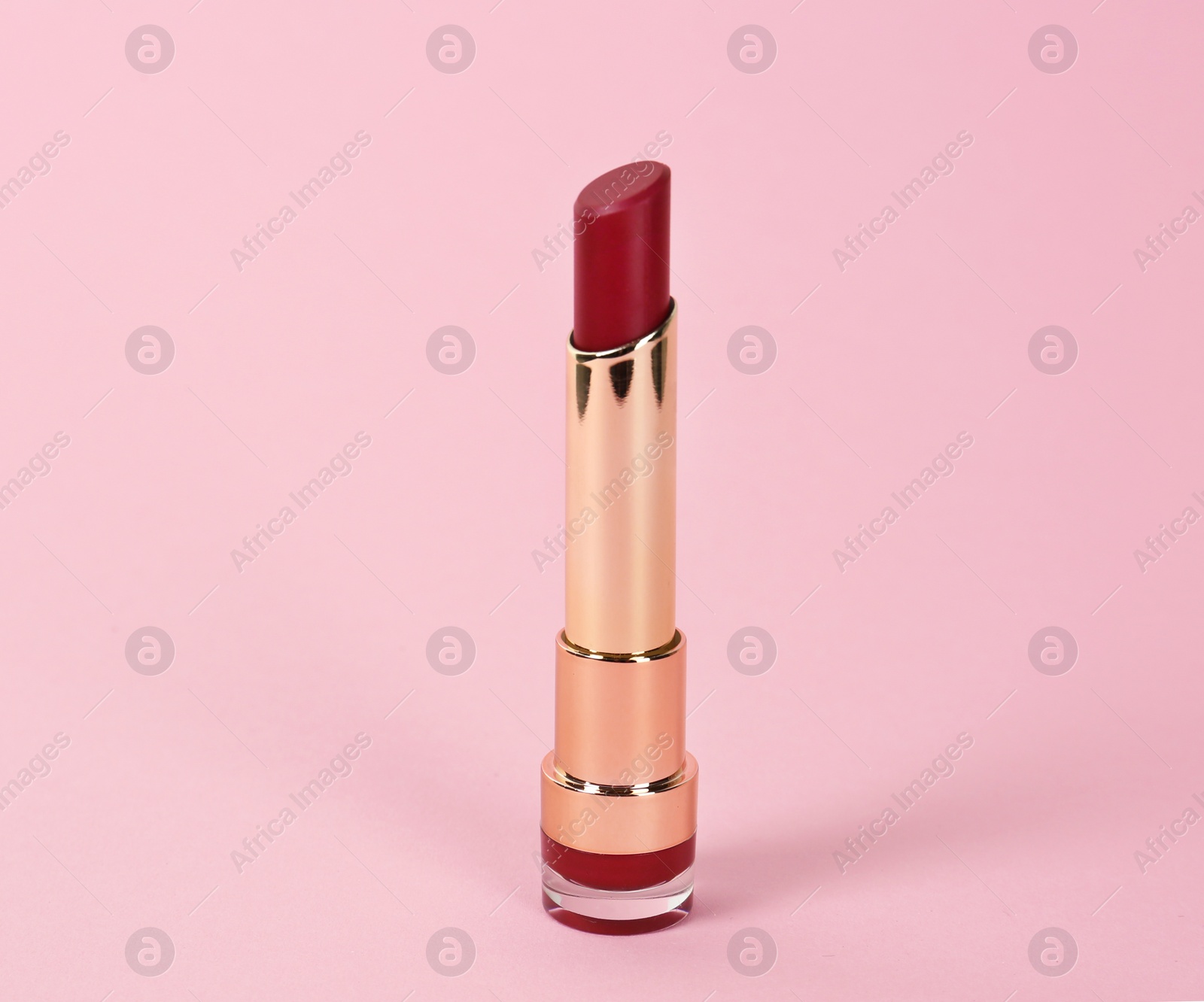 Photo of Bright lipstick in gold tube on pink background