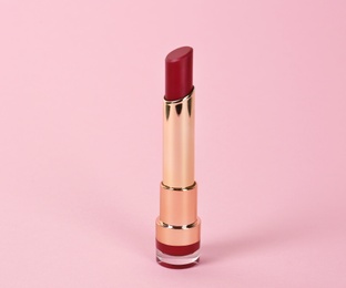 Photo of Bright lipstick in gold tube on pink background
