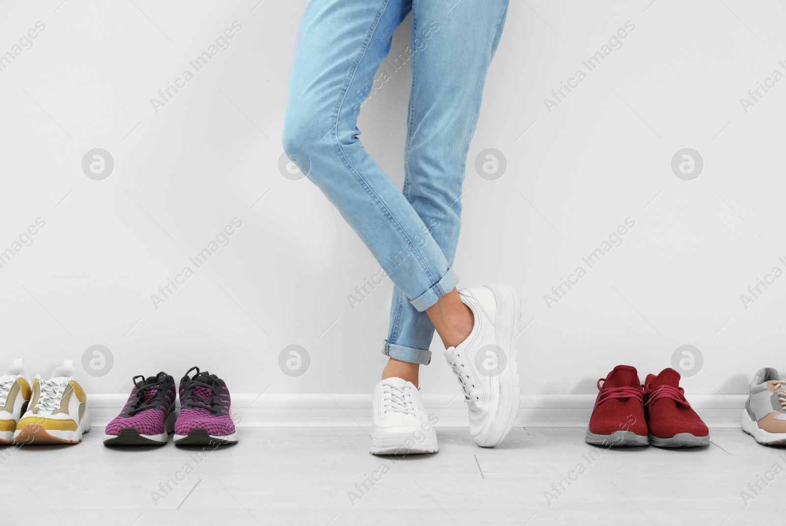 Photo of Woman trying on different shoes near white wall, closeup