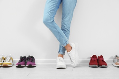 Woman trying on different shoes near white wall, closeup