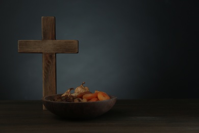 Photo of Cross and dried fruits on wooden table, space for text. Lent season