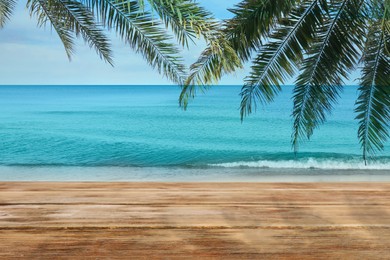 Wooden table under green palm leaves near ocean