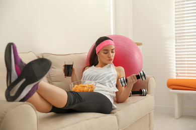 Photo of Lazy young woman with sport equipment and junk food at home